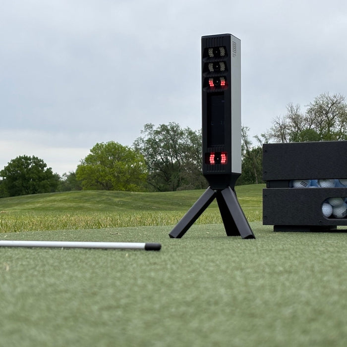 The Square Golf Omni golf launch monitor with alignment stick and golf balls at the driving range