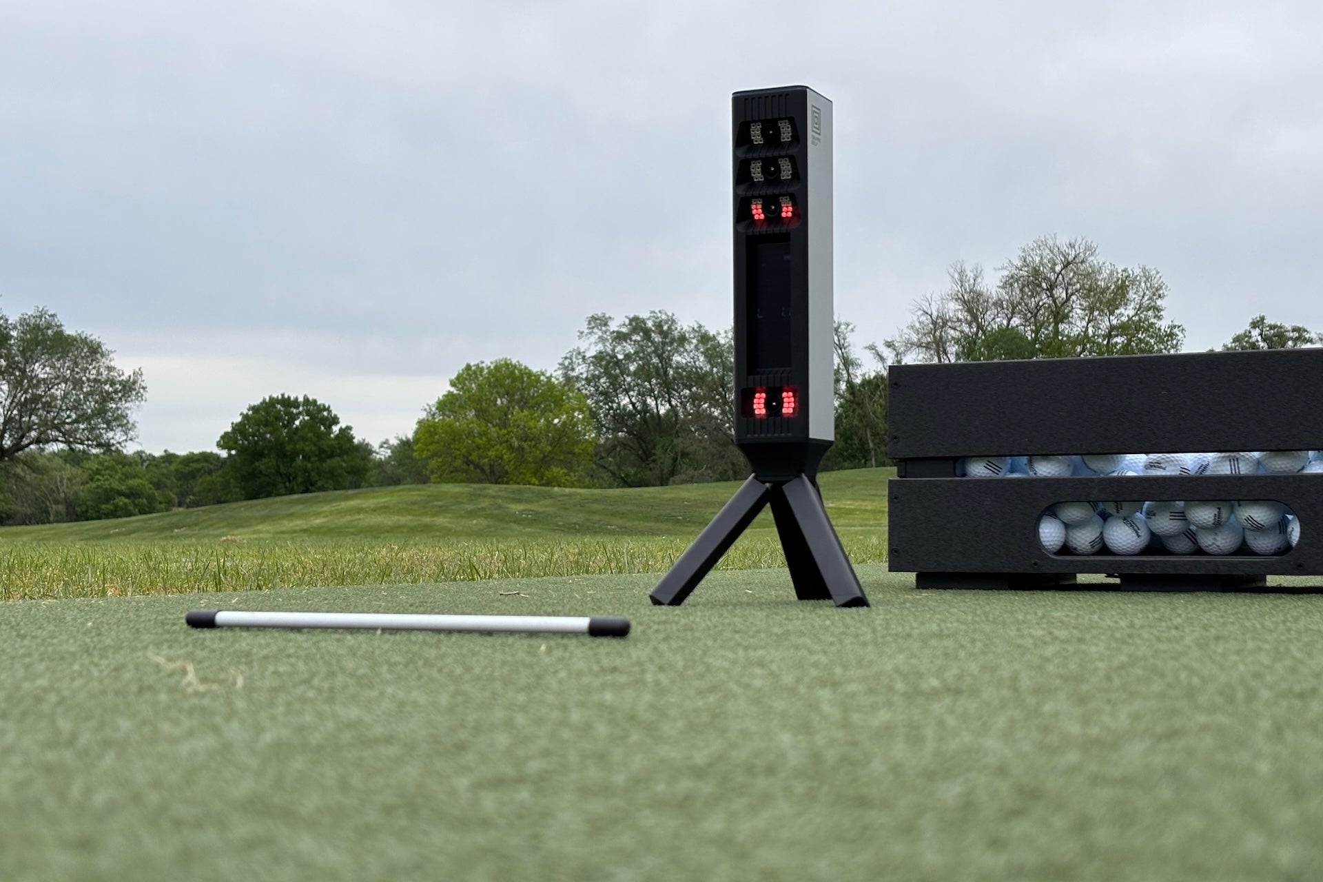 The Square Golf Omni golf launch monitor with alignment stick and golf balls at the driving range