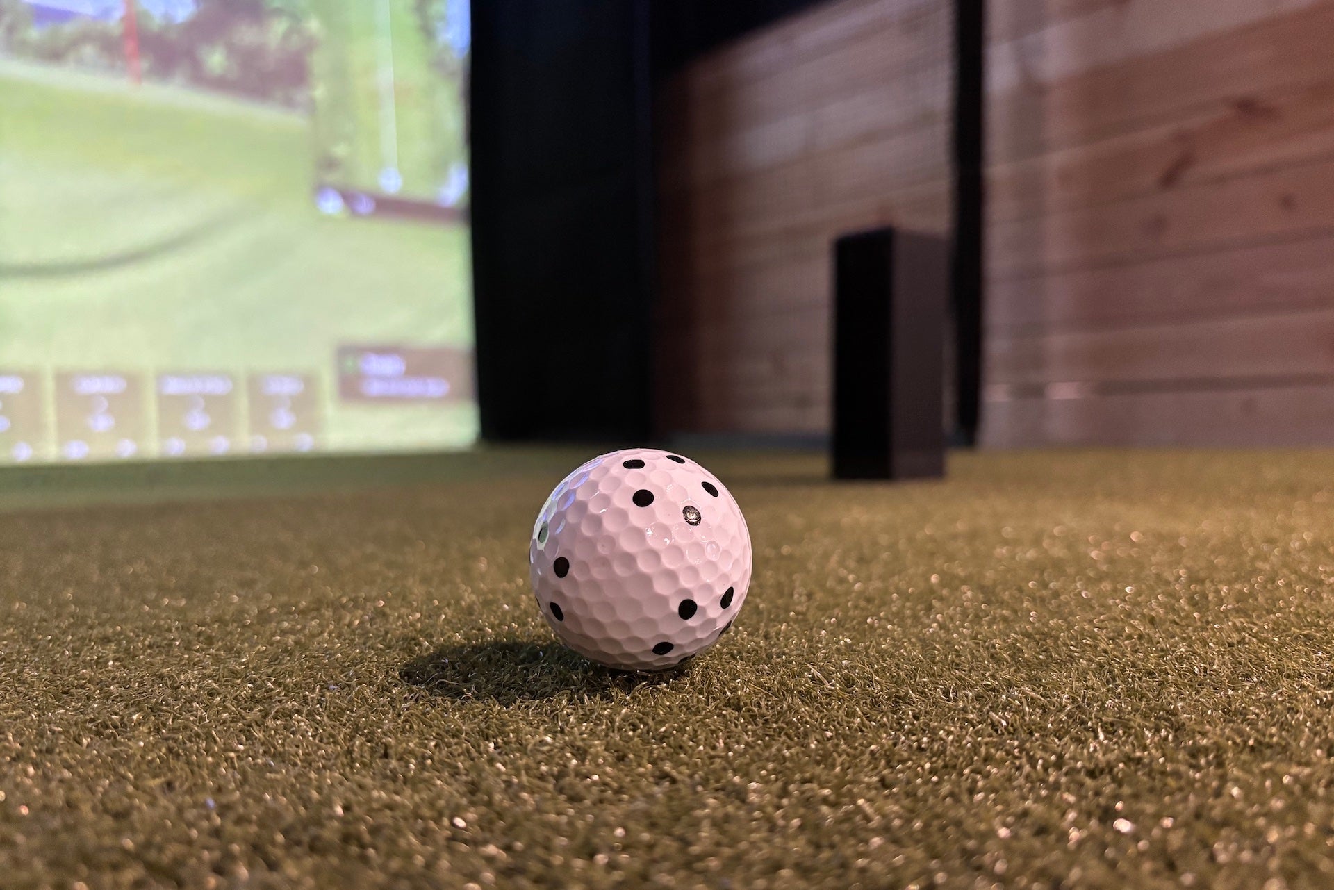 A RCT ball on a golf hitting mat in front of a Square Golf launch monitor and impact screen with virtual golf course on it