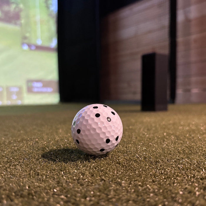 A RCT ball on a golf hitting mat in front of a Square Golf launch monitor and impact screen with virtual golf course on it