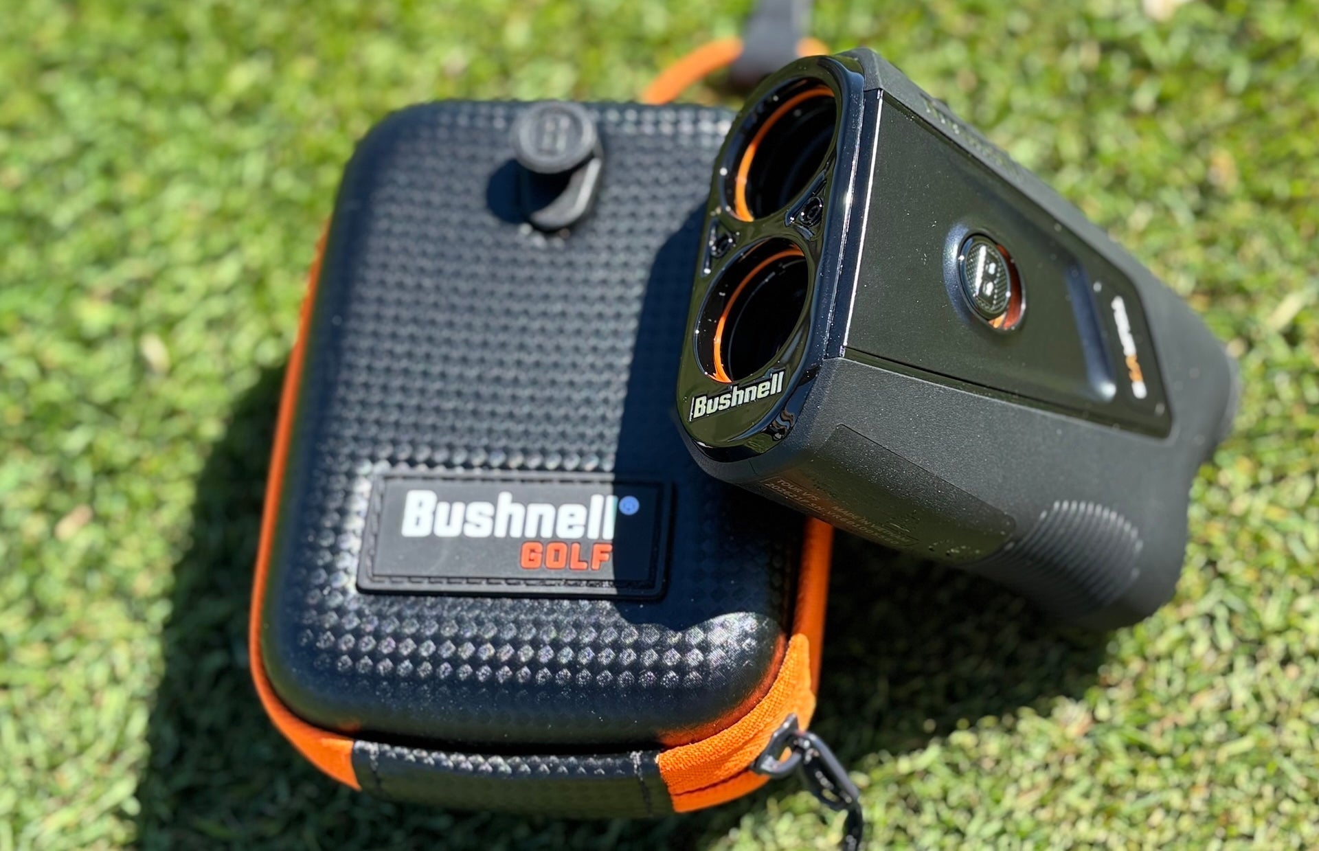 The Bushnell Tour V7 Shift rangefinder propped on the carrying case on the grass at the range