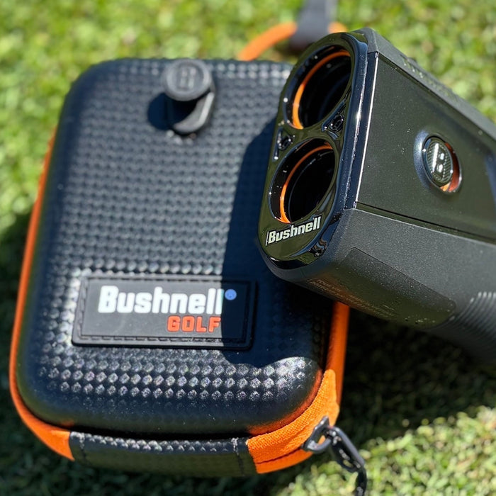 The Bushnell Tour V7 Shift rangefinder propped on the carrying case on the grass at the range