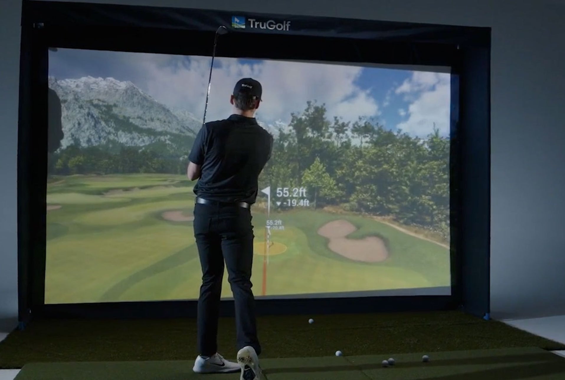 A golfer post swing in a TruGolf golf simulator