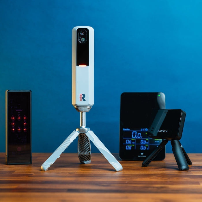 Group photo of Square, Rapsodo MLM2PRO, Swing Caddie SC4 Pro and Garmin R10 on a woodgrain surface against a blue background