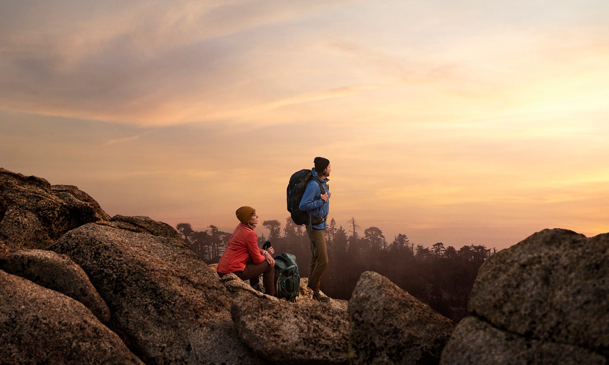 Two hikers with backpacks watching the sunset on a rocky cliff with
