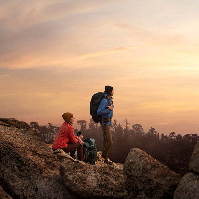 Two hikers with backpacks watching the sunset on a rocky cliff with