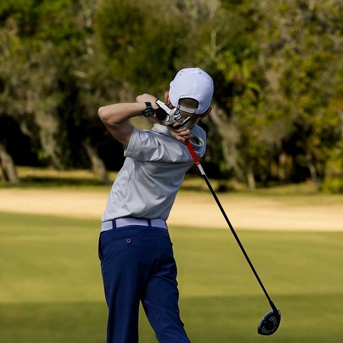 A young golfer post swing at the tee on a golf course wearing the Garmin Approach J1 golf GPS watch