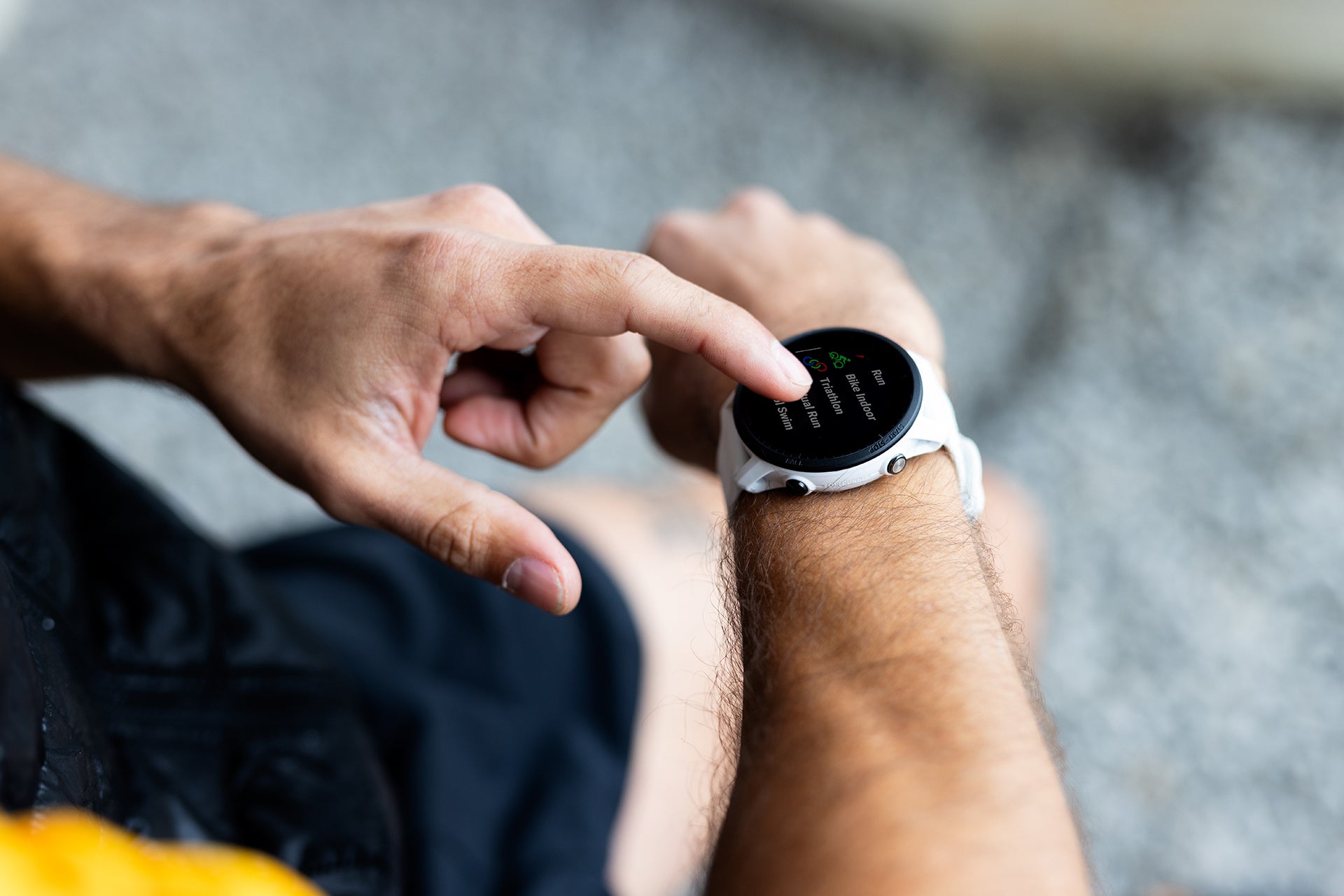 A white Garmin Forerunner 955 on the wrist of a runner who is touching the touchscreen display with a finger