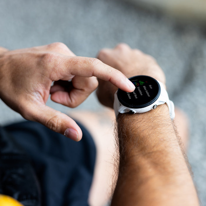 A white Garmin Forerunner 955 on the wrist of a runner who is touching the touchscreen display with a finger