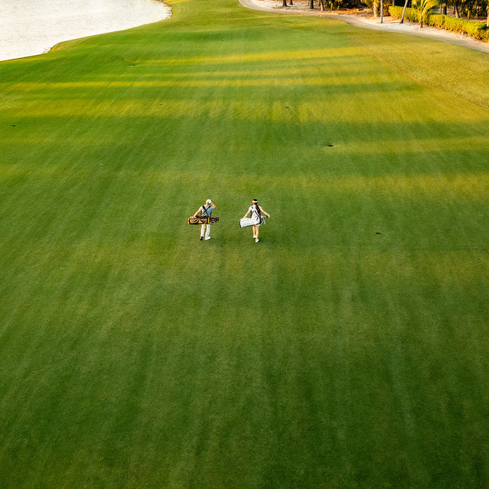 A wide shot of a golf fairway with two people walking up the middle and a sand trap on the left