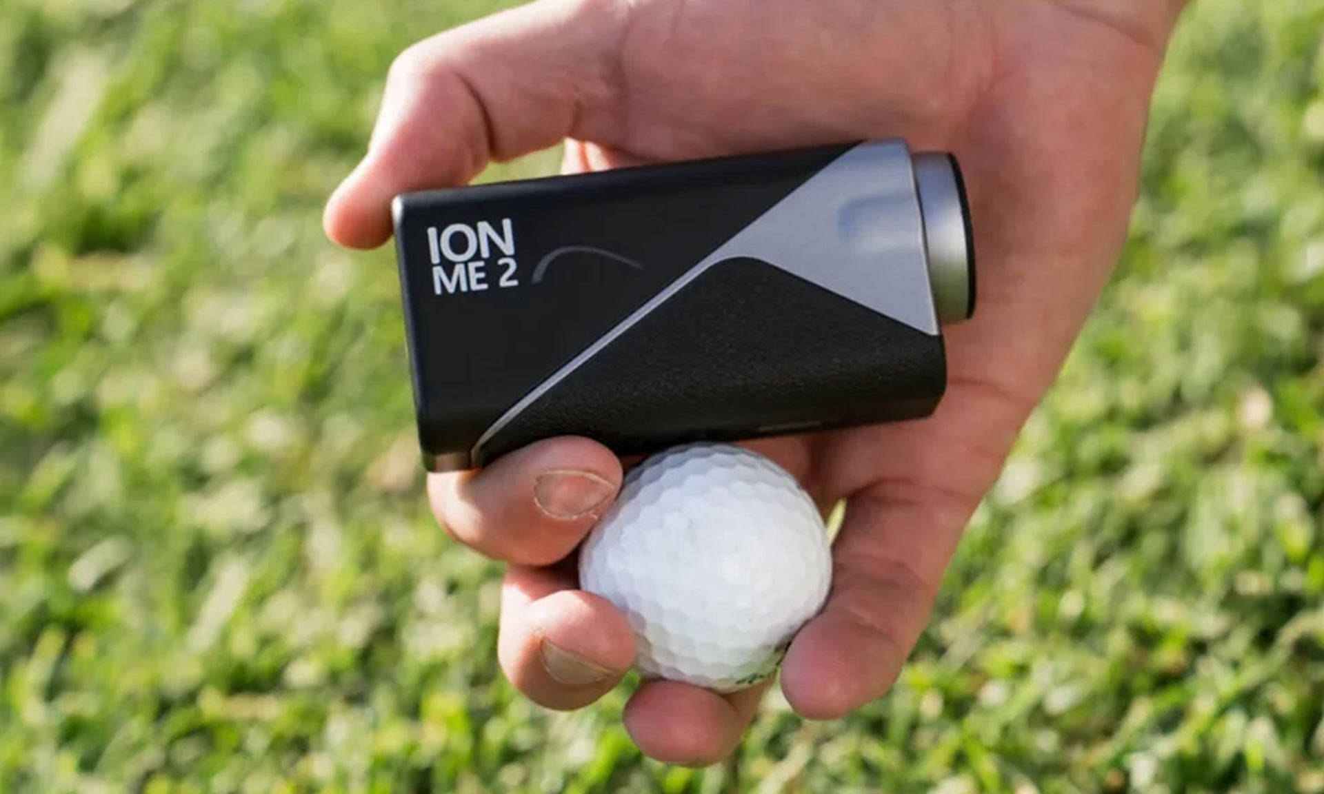 The Mileseey IONME2 rangefinder in a hand with a golf ball over some grass