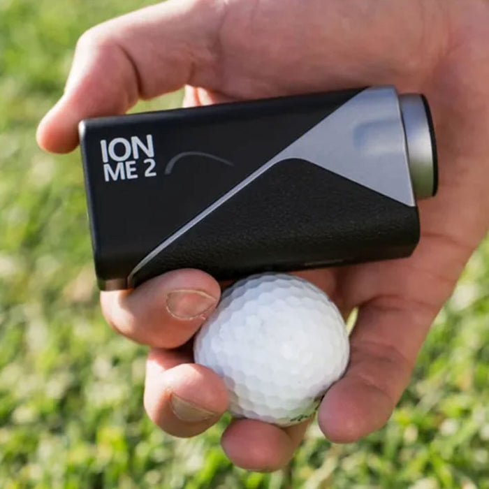 The Mileseey IONME2 rangefinder in a hand with a golf ball over some grass