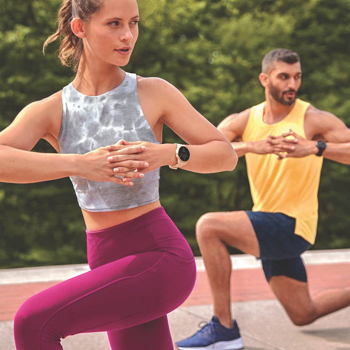 A woman and man doing knee bends outdoors while wearing Garmin Venu 2 Plus watches