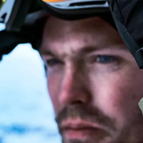 A man dressed in winter wear getting ready to pull down goggles with an orange-strapped Garmin fenix 7 watch on his wrist