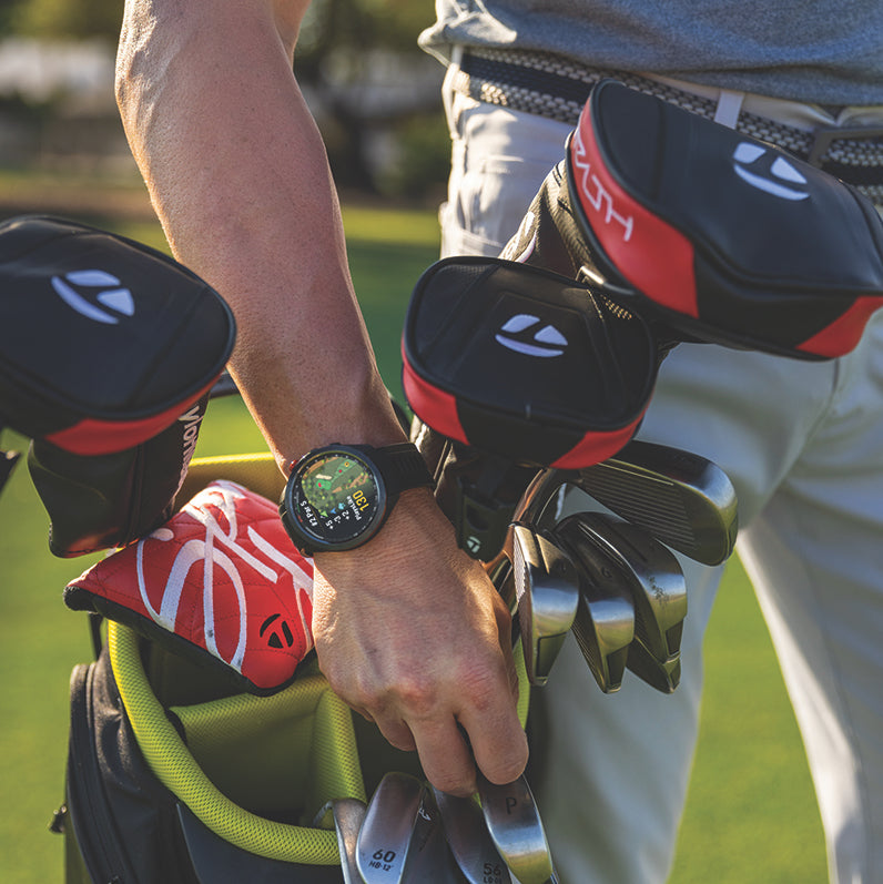 A man wearing a Garmin Approach S70 golf watch as he grabs an iron from his golf bag while on the course