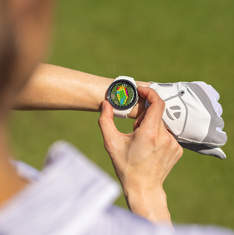 A female golfer wearing a 42 mm Garmin Approach S70 golf watch with Green Contours on the display
