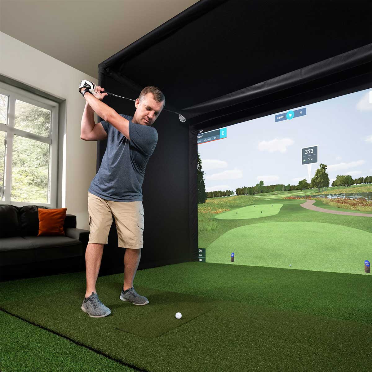 A golfer in his backswing getting ready to hit a golf ball into a Carl's Place enclosure in his home golf simulator with a virtual golf game on the impact screen.