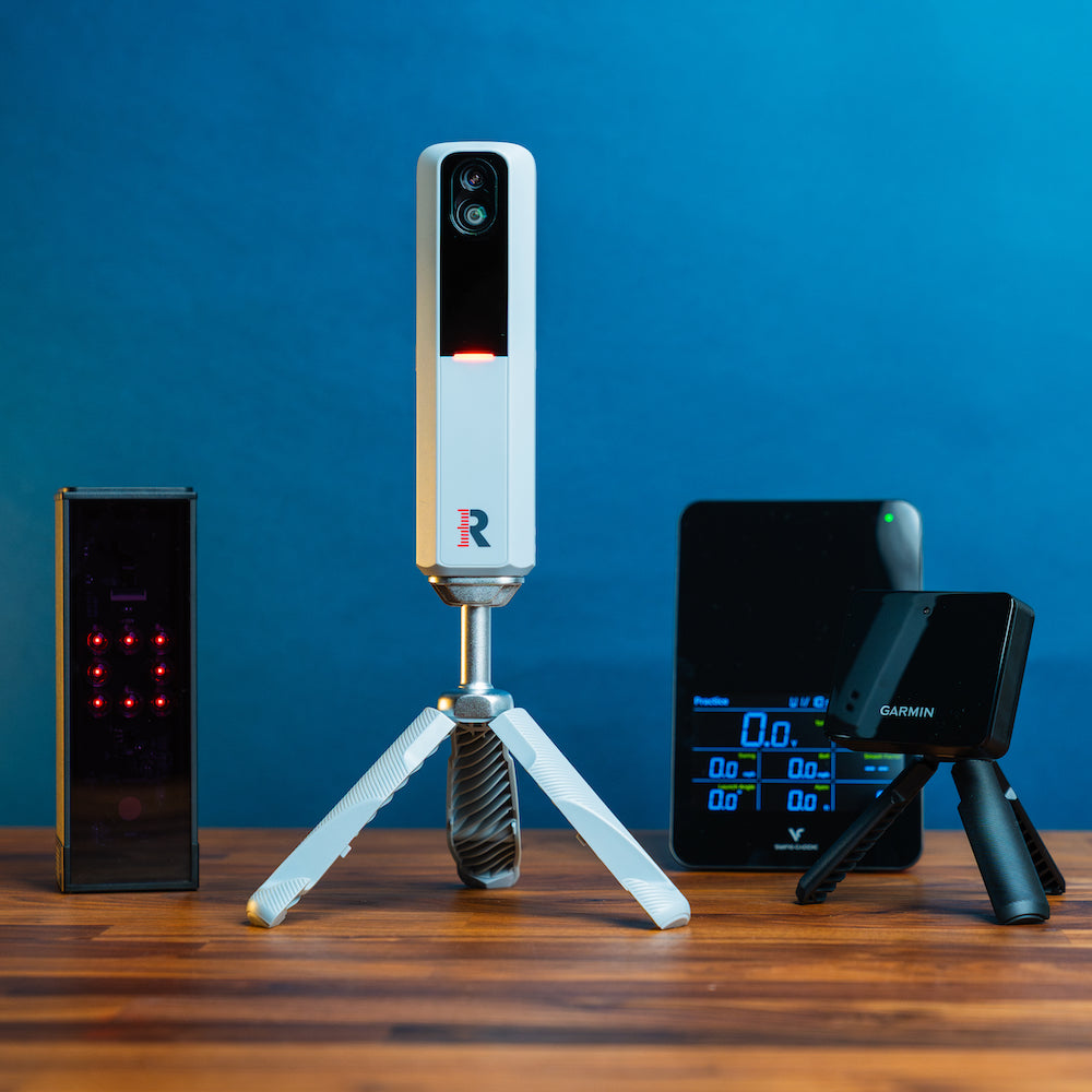 The Square, Rapsodo MLM2PRO, Swing Caddie SC4 Pro, and Garmin Approach R10 golf launch monitors together on a woodgrain surface against a blue background