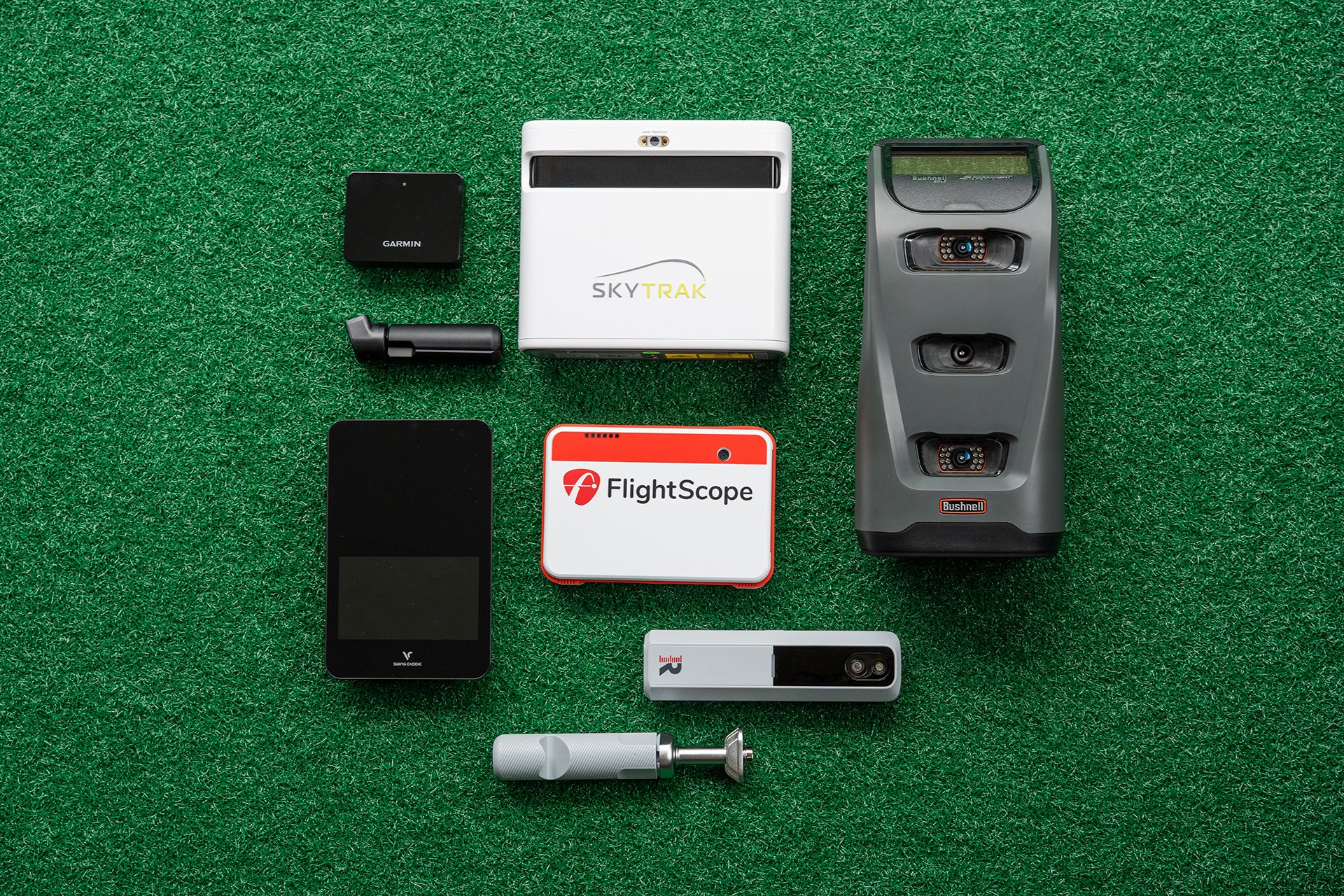 Several PlayBetter golf launch monitors—SkyTrak+, Bushnell Launch Pro, Swing Caddie SC4, Rapsodo MLM2PRO, FlightScope Mevo+ and Garmin Approach R10 picture flat on green turf