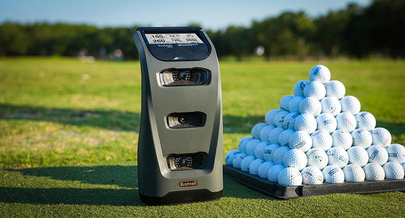 Bushnell Launch Pro golf launch monitor next to a pyramid of golf balls at the range