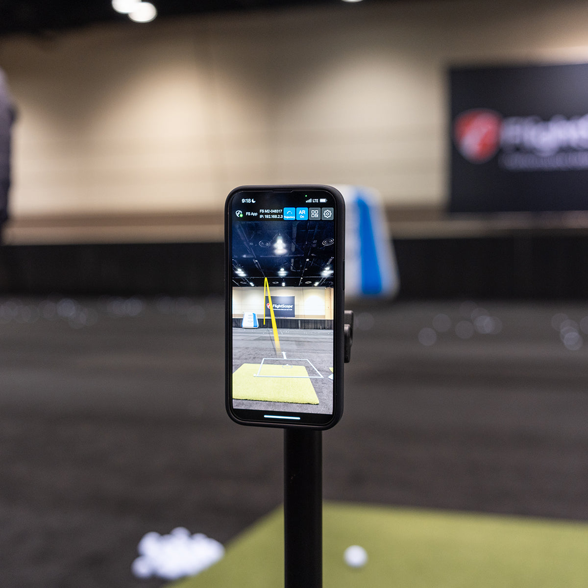 A phone on a stand set up on an indoor golf range with FlightScope tracer software showing a golf shot