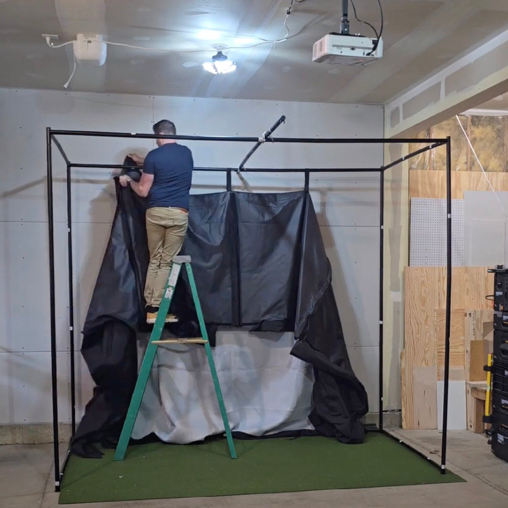 A man assembling a PlayBetter SimStudio on his own, standing on a ladder and attaching the enclosure to the frame