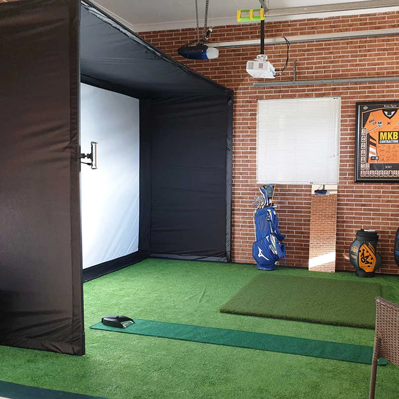 A golfer in the PlayBetter SimStudio set up with golf simulator bay enclosure, impact screen, projector, golf hitting mat, putting green, and golf bags and gear