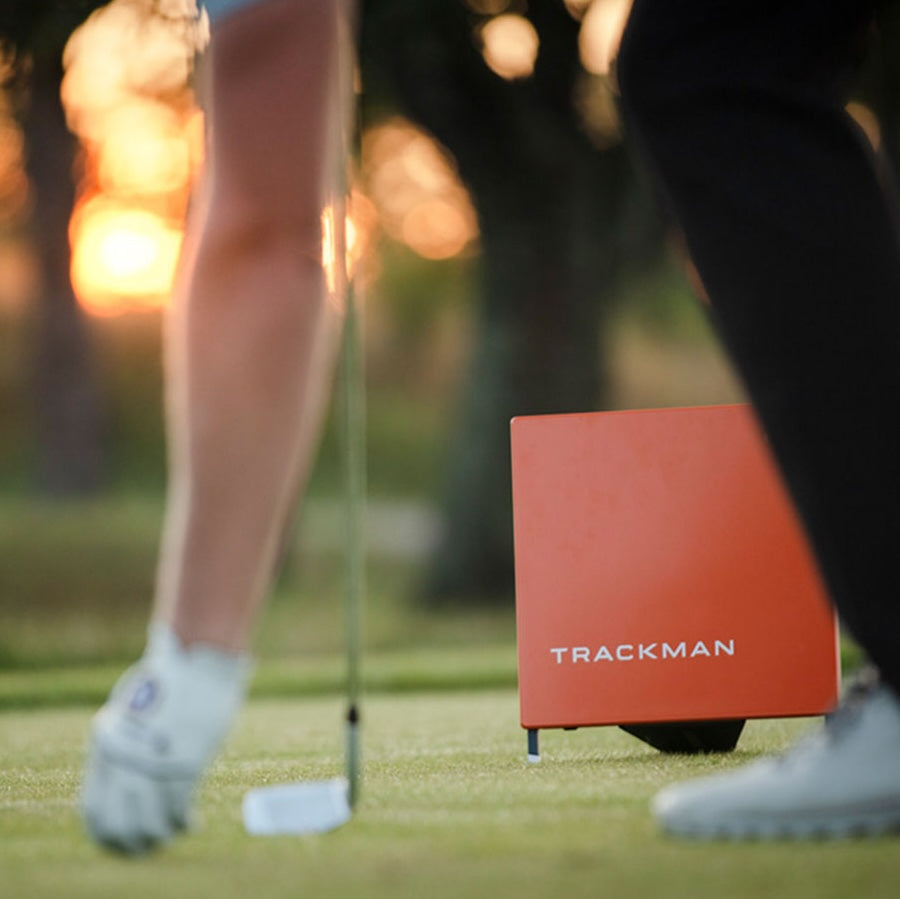 The Trackman Launch Monitor and Golf Simulator behind a golfer on the course placing a golf ball on the grass