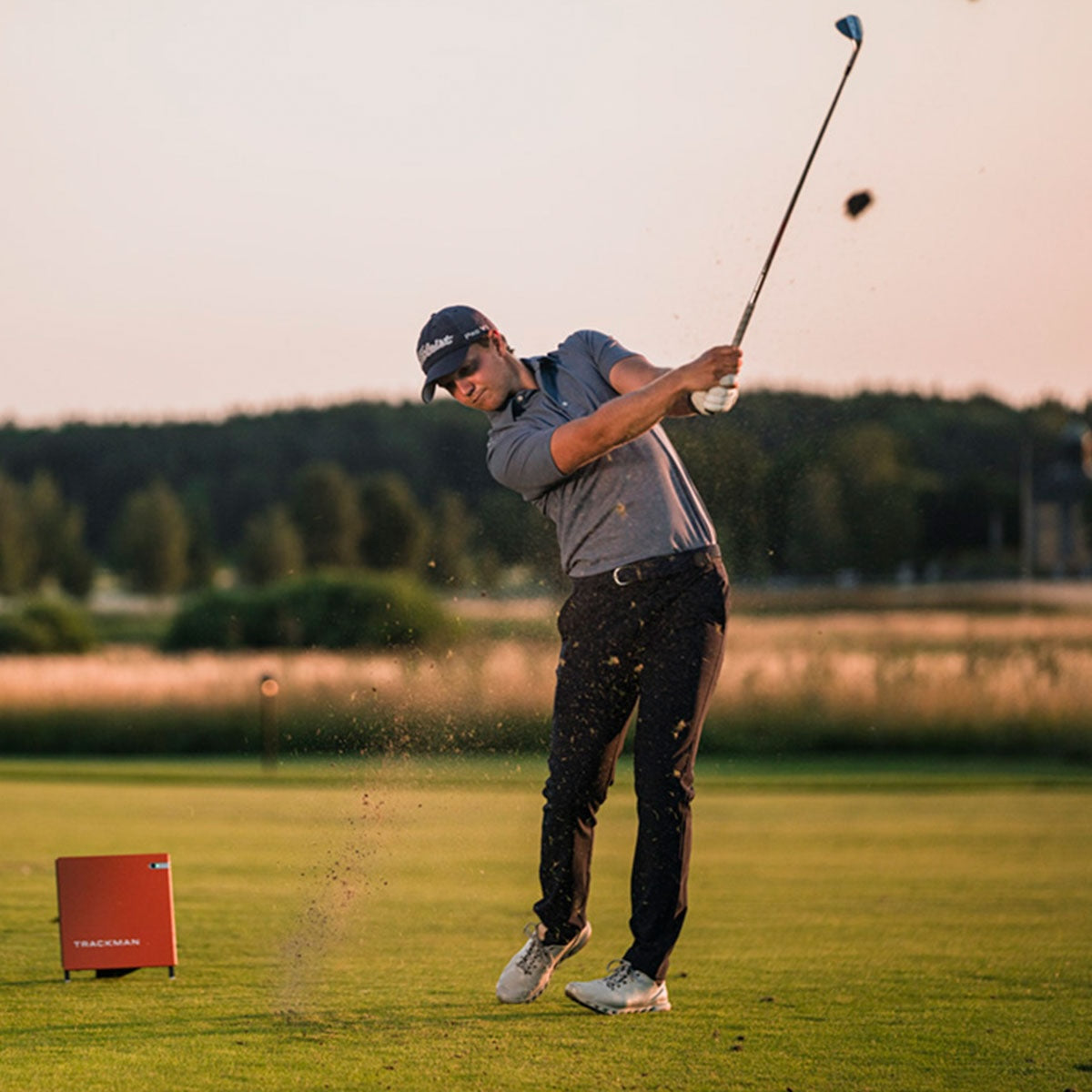 Golfer swinging a club on a golf course in front of a Trackman 4 golf launch monitor