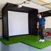 A golfer standing on a golf hitting mat holding a club looking down a the golf ball in front of a PlayBetter SimStudio