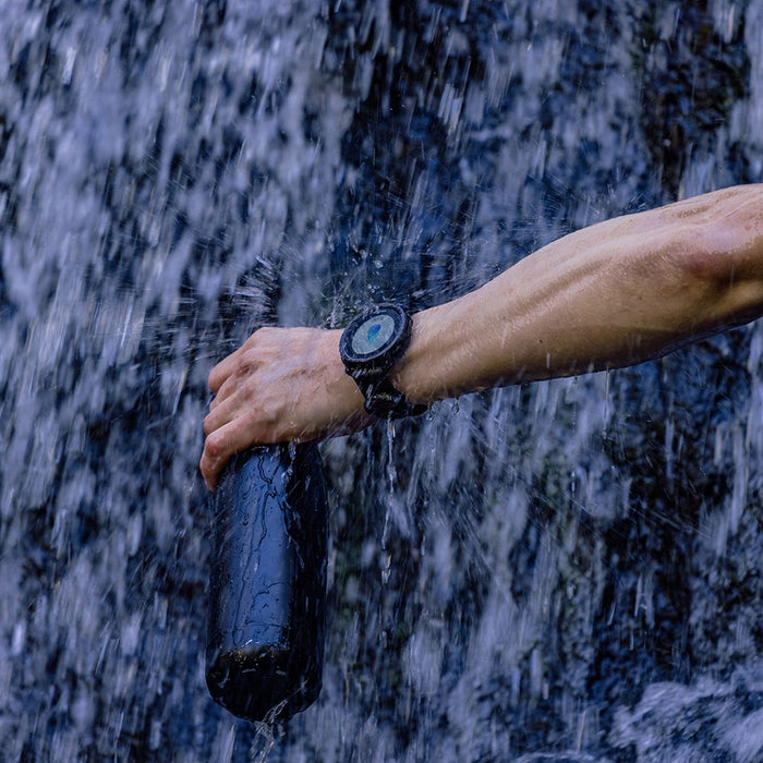 A hiker refilling his water bottle in the falls while wearing the black version of Polar Grit X